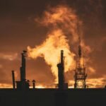Silhouette of industrial plant smokestacks against a dramatic sunset sky.